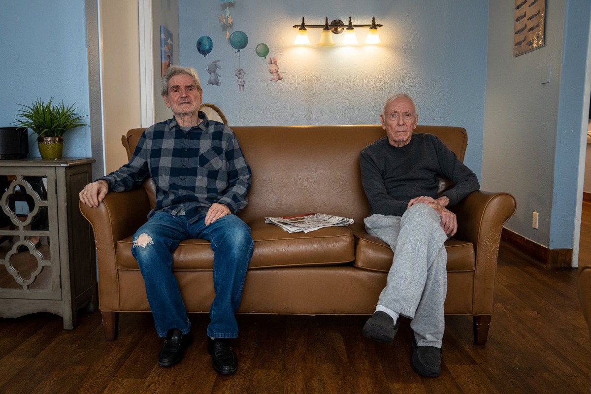 Two elderly men sitting on a couch in a living room.