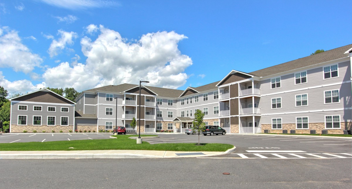 A modern residential apartment complex with a spacious parking lot under a clear, blue sky.