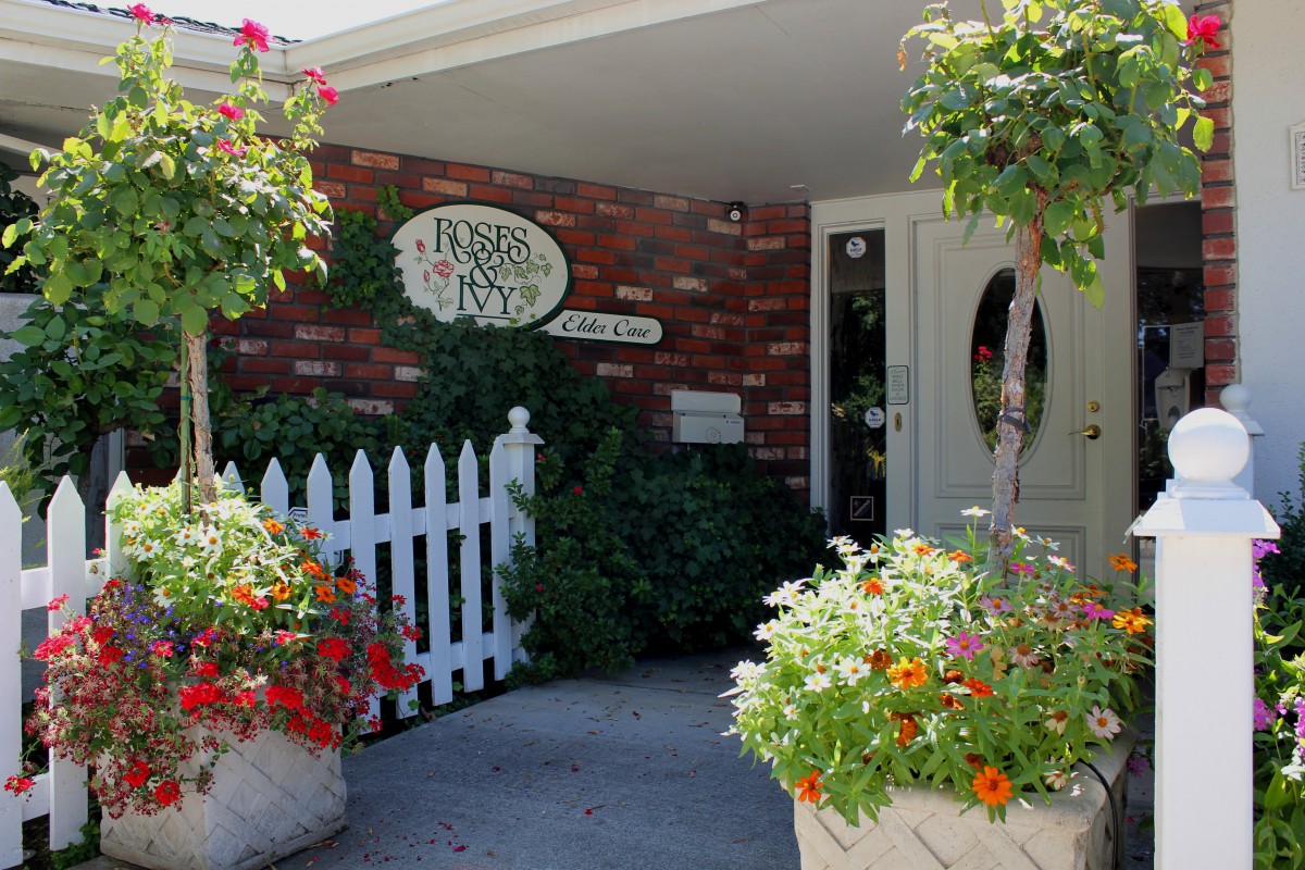A welcoming entrance to a building with a brick exterior, adorned with colorful flowers and a white picket fence.