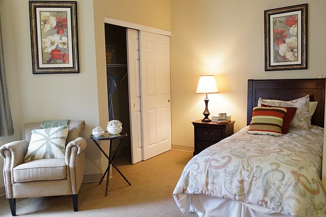A cozy bedroom featuring a bed, nightstand with a lamp, and framed artwork.