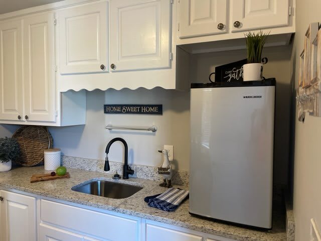 A compact kitchen area with a sink, countertop, mini fridge, and cabinets.