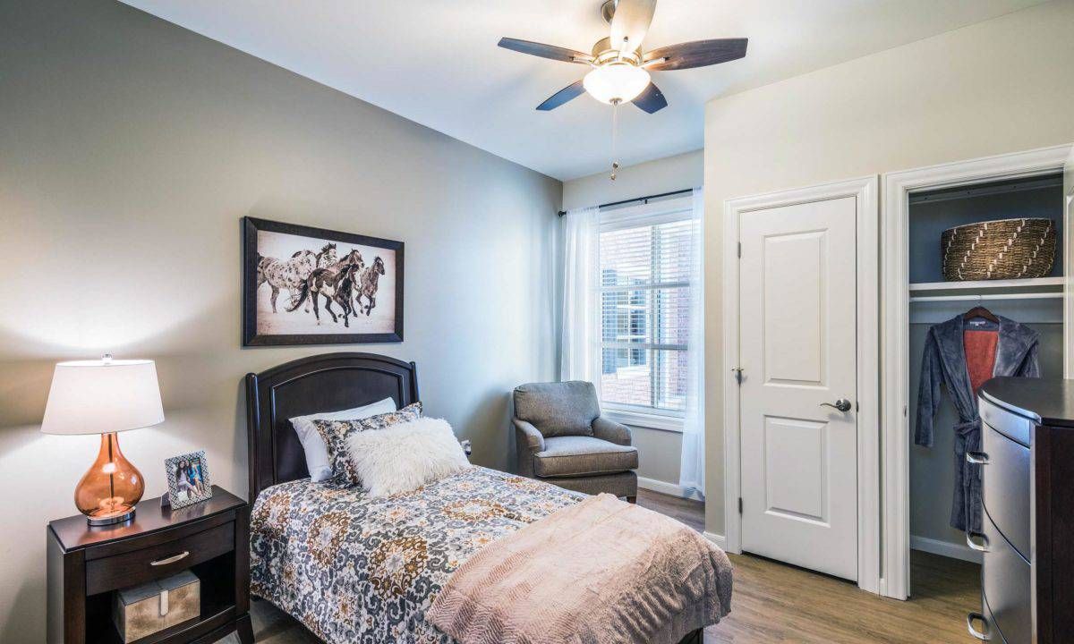 A cozy bedroom with a single bed, armchair, and ceiling fan.