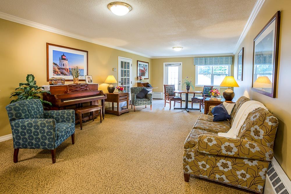 A cozy living room with a piano, seating area, and dining space, illuminated by warm lighting.