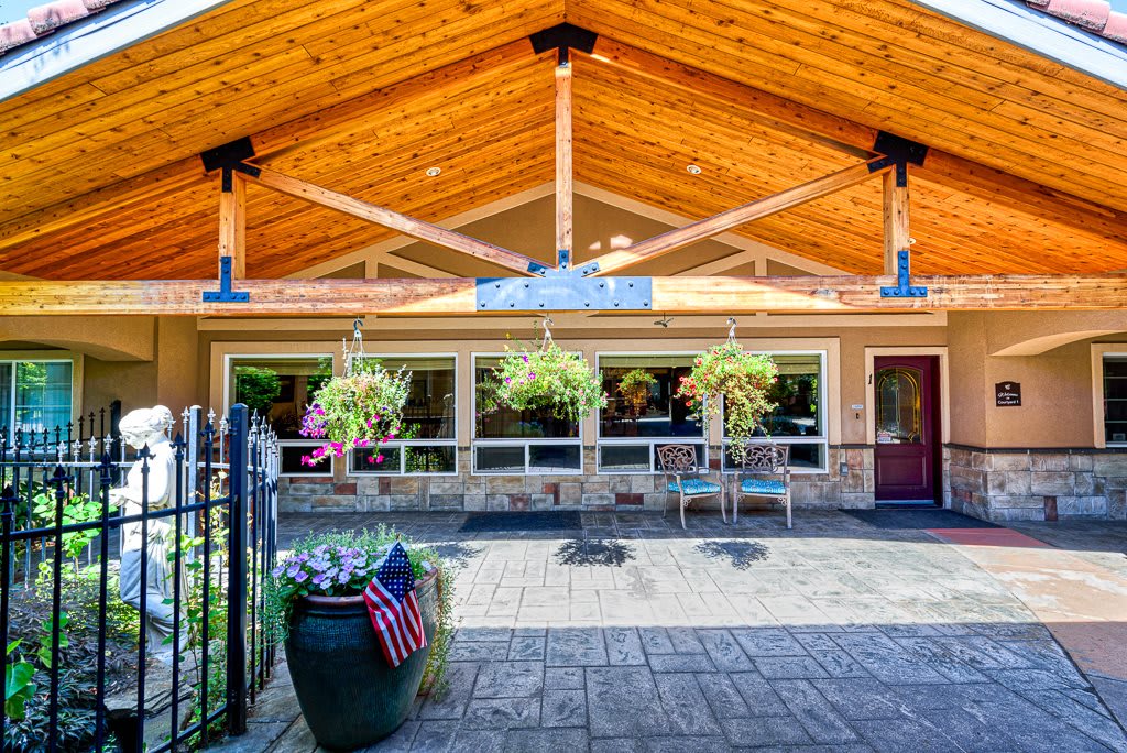 The entrance of a building featuring a wooden roof and outdoor seating, adorned with plants.
