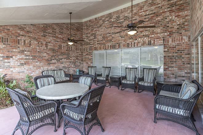 An outdoor patio area with wicker furniture and ceiling fans against a brick wall.
