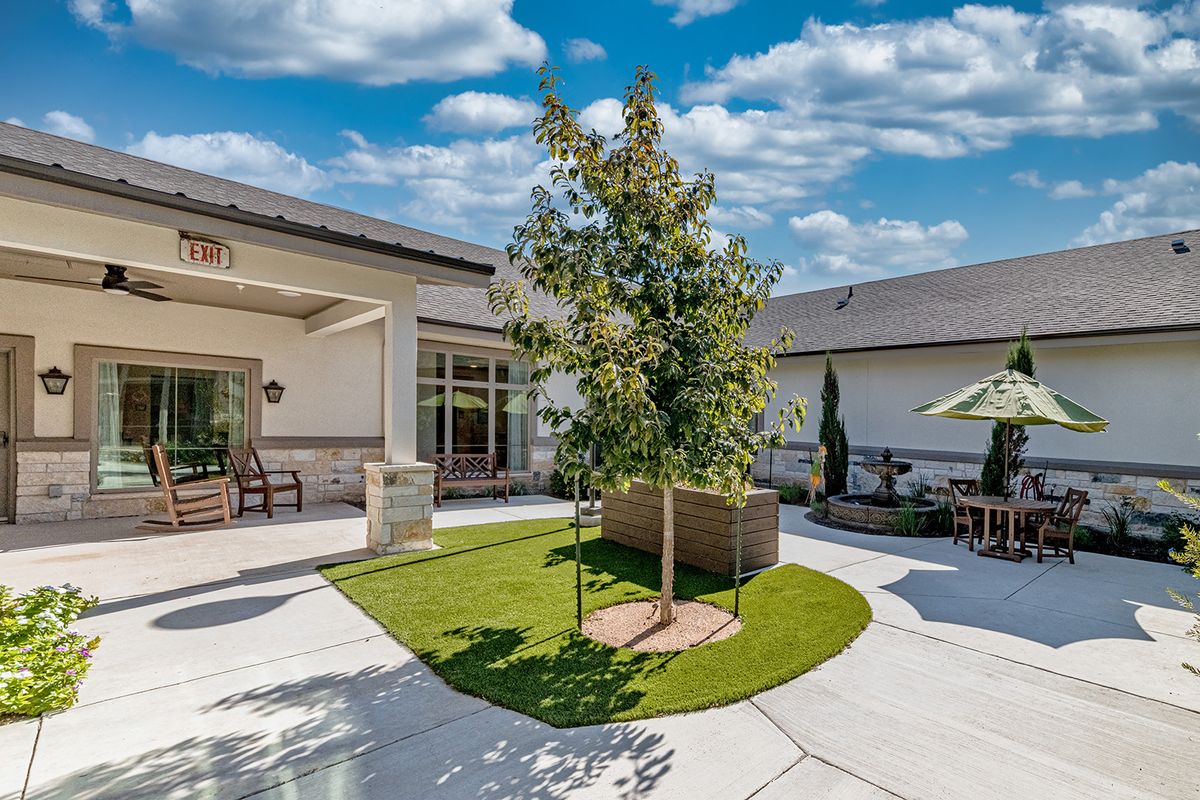A well-maintained backyard featuring a central tree with surrounding grass and patio space.