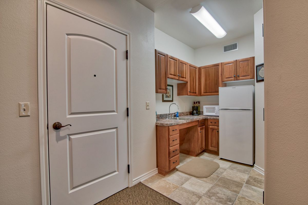 A compact apartment kitchen with wooden cabinets, a refrigerator, and essential appliances.