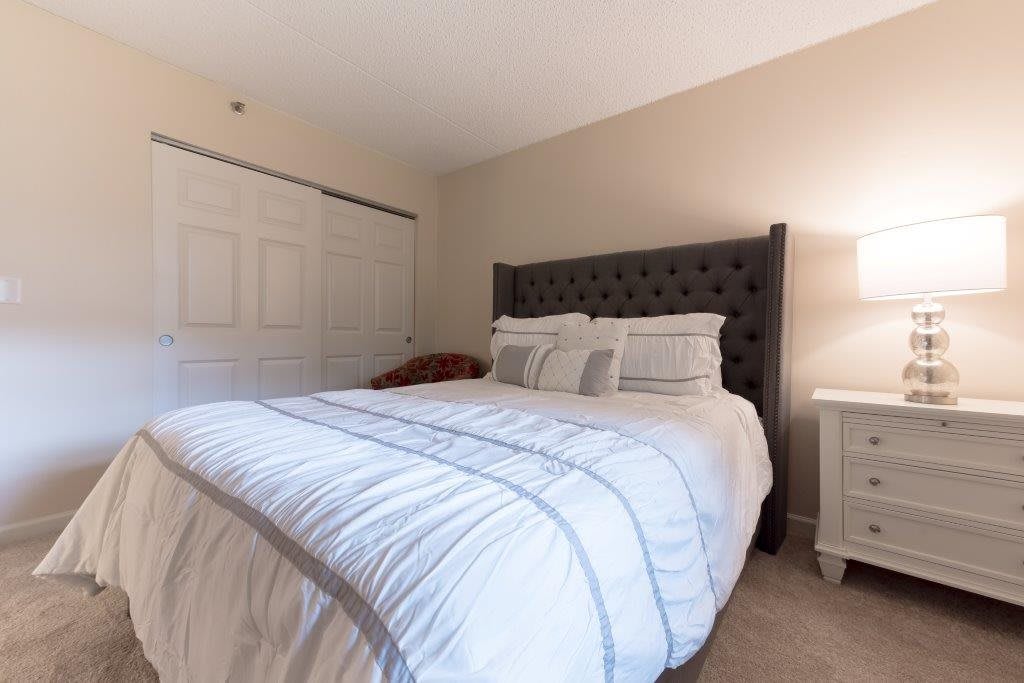 A cozy bedroom with a neatly made bed, featuring a tufted headboard and soft lighting from a bedside lamp.