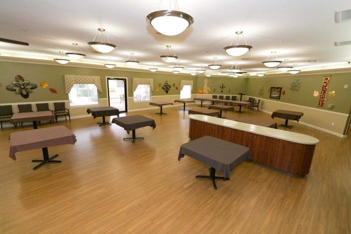 An empty room with tables, bright lighting, and wooden flooring.
