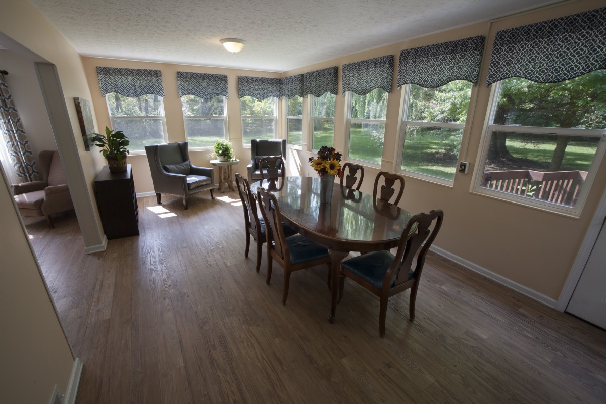 A bright dining area with a wooden table and chairs, surrounded by large windows.