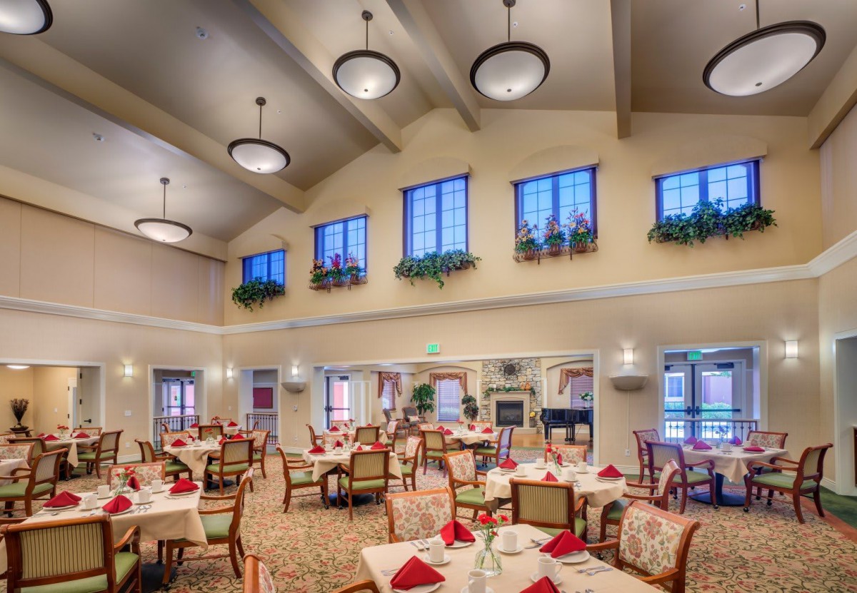 A spacious and elegantly decorated dining room with neatly arranged tables and chairs, illuminated by overhead chandeliers.
