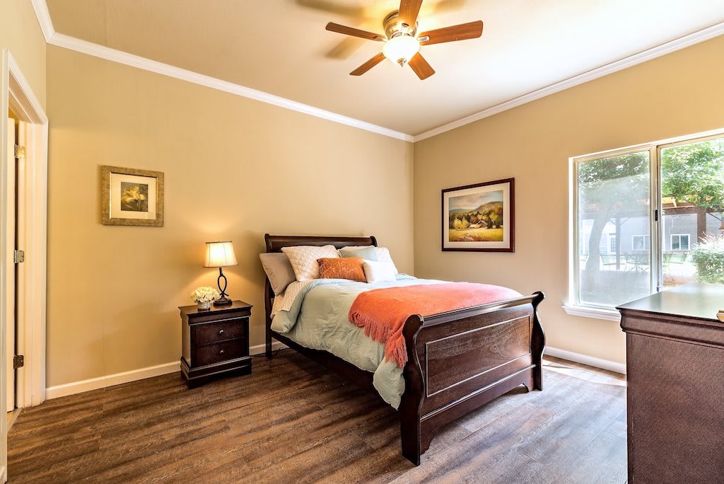 A cozy bedroom with a wooden bed, side table lamp, and ceiling fan.