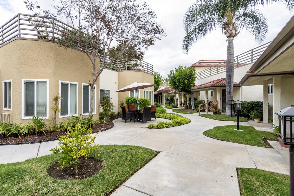 A well-maintained residential courtyard featuring landscaped pathways, palm trees, and outdoor seating.
