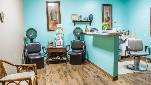 A cozy salon waiting area with turquoise walls and decorated with framed art and comfortable seating.