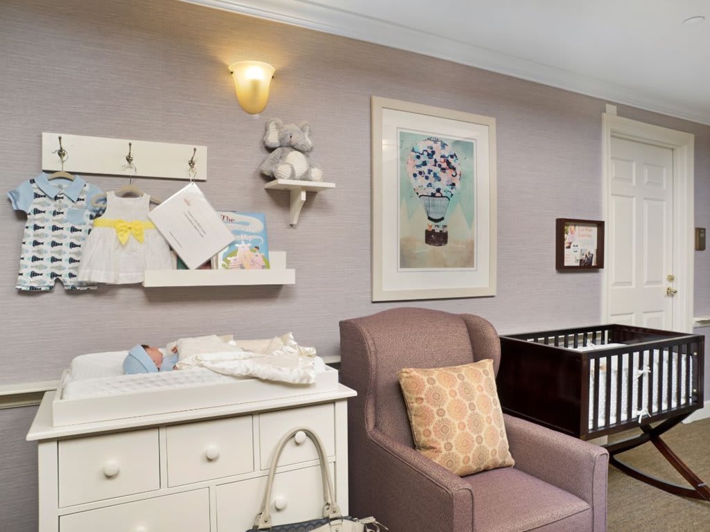A cozy nursery with a changing table, armchair, and crib, decorated with wall art and shelves.