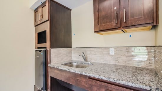 A modern kitchen area featuring a granite countertop, sink, and wooden cabinets.