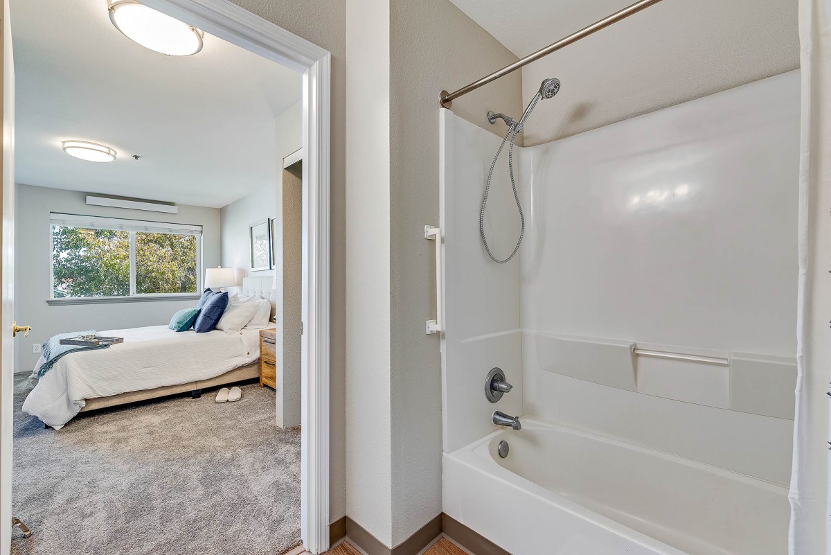 A bathroom with a bathtub and shower next to a bright and cozy bedroom.