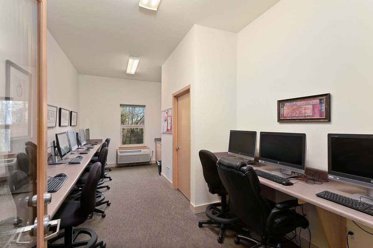 An empty computer lab with multiple workstations and chairs arranged in rows.