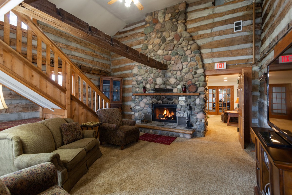 A cozy rustic cabin living room featuring a large stone fireplace and wooden beams.