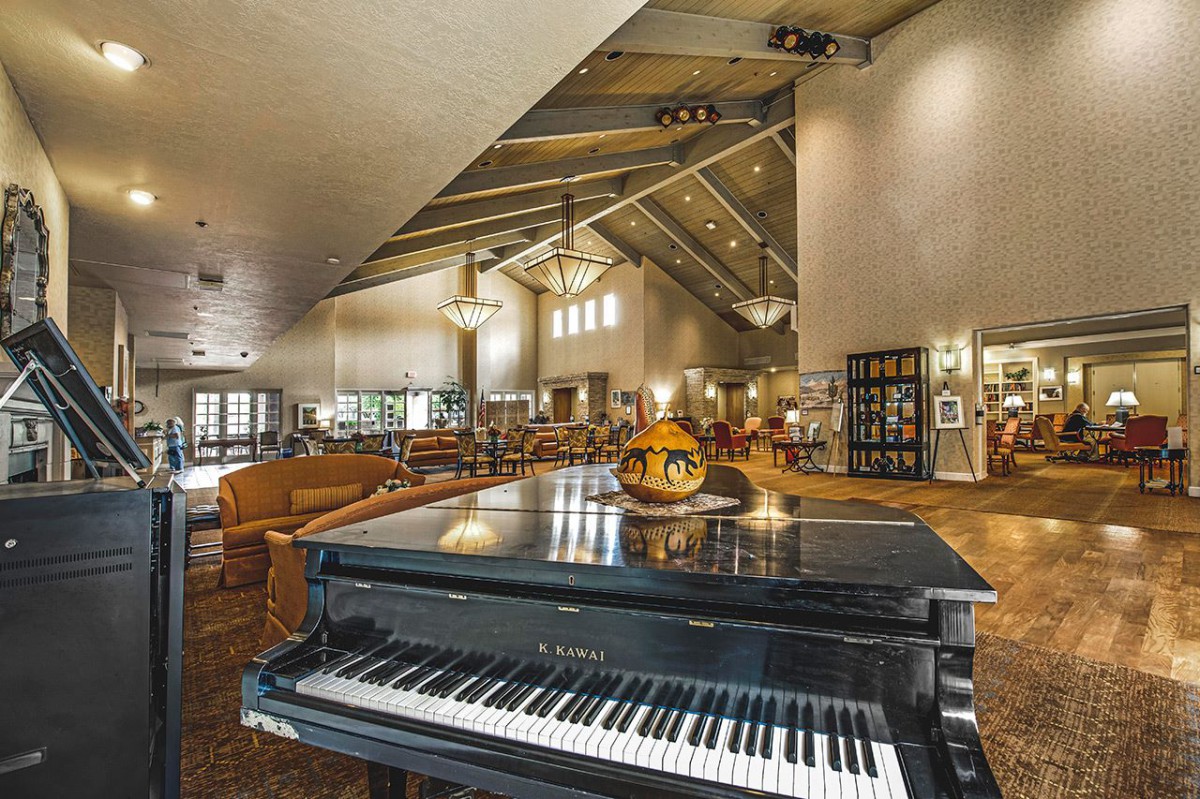 A spacious lounge area featuring a grand piano with elegant lighting and modern furnishings.