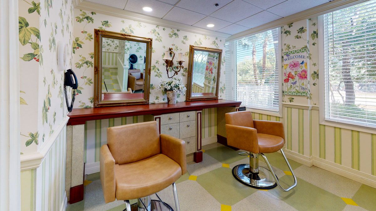 A cozy salon interior featuring two tan salon chairs with mirrors on the wall and floral wallpaper.