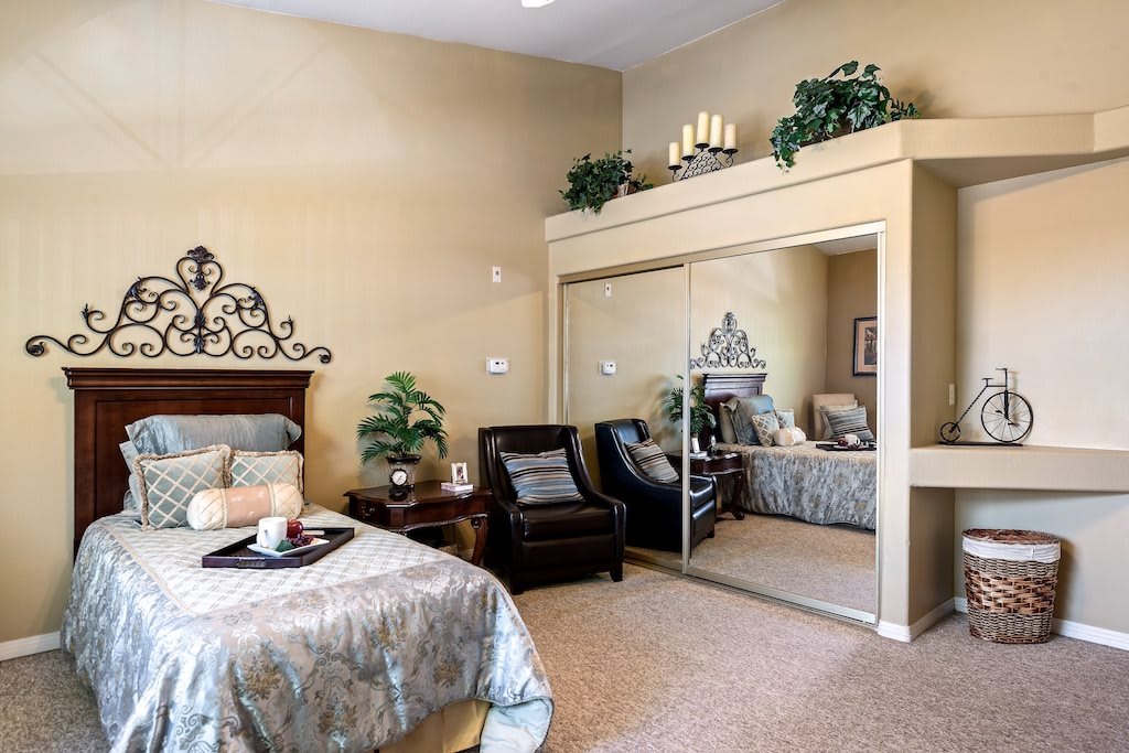 A cozy bedroom with elegant decor, featuring a bed, armchair, mirrored closet, and indoor plants.