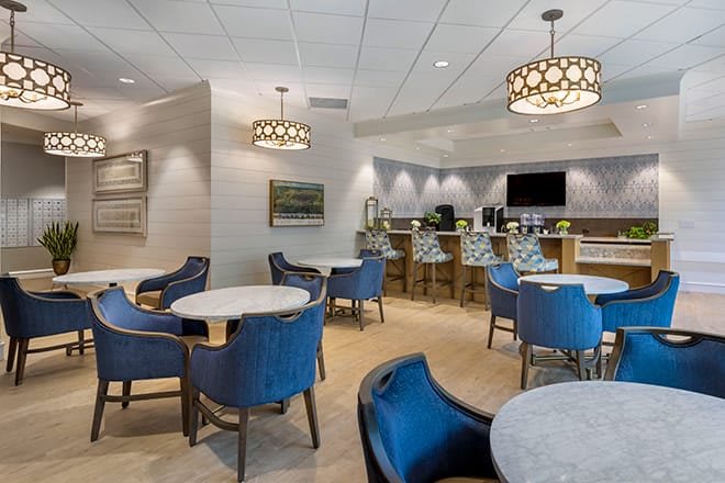 A modern lounge with blue upholstered chairs, round tables, and stylish pendant lighting.