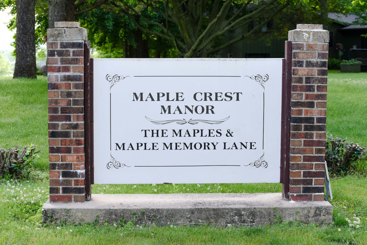A sign for Maple Crest Manor, with mentions of The Maples and Maple Memory Lane, surrounded by greenery.