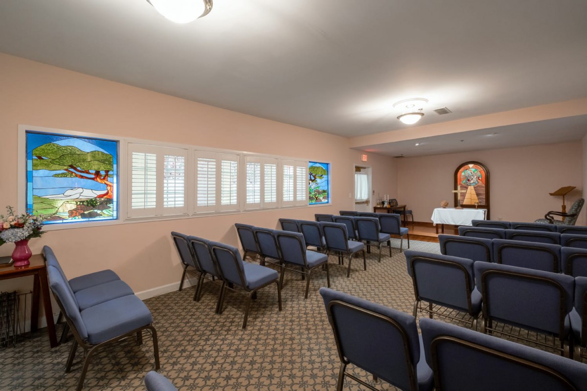 A meeting room with rows of chairs, stained glass windows, and a decorated altar.