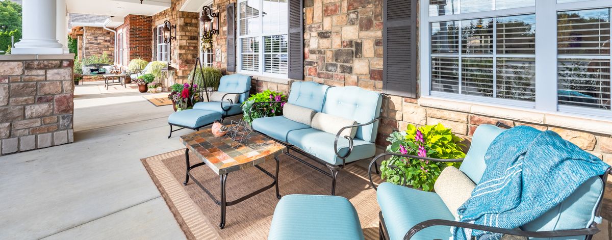 A cozy outdoor patio with cushioned seating and a coffee table, surrounded by decorative plants.