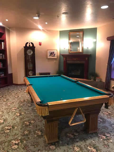 A cozy room featuring a billiards pool table, a tall clock, and a fireplace.