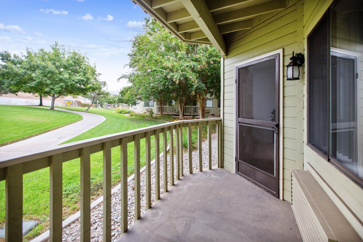 A cozy patio with a wooden railing overlooking a lush, green yard.
