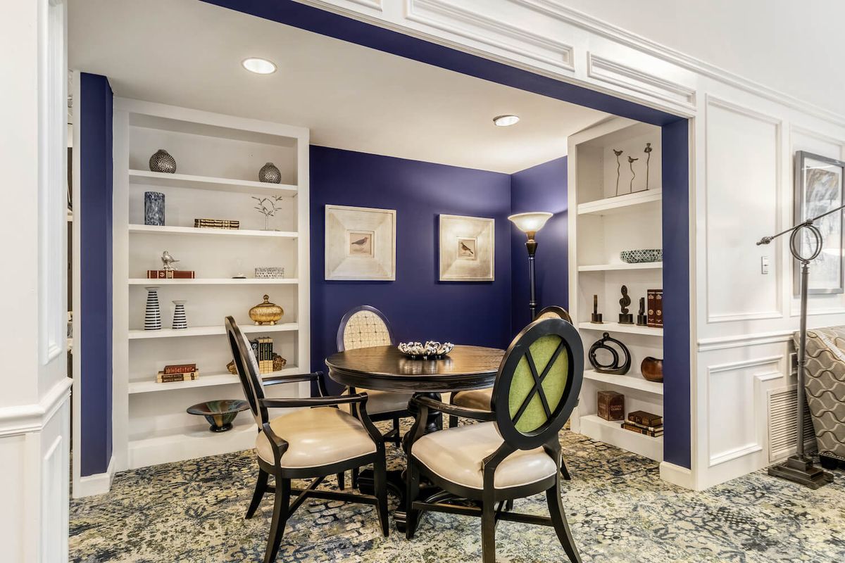 A cozy dining area with elegant furniture and built-in bookshelves against a striking blue accent wall.