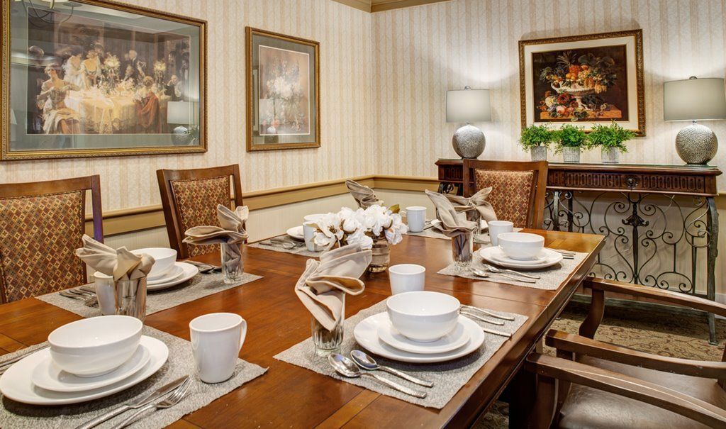 A warmly lit dining room with a neatly arranged table setting, featuring elegant dishware and decorative artwork on the walls.