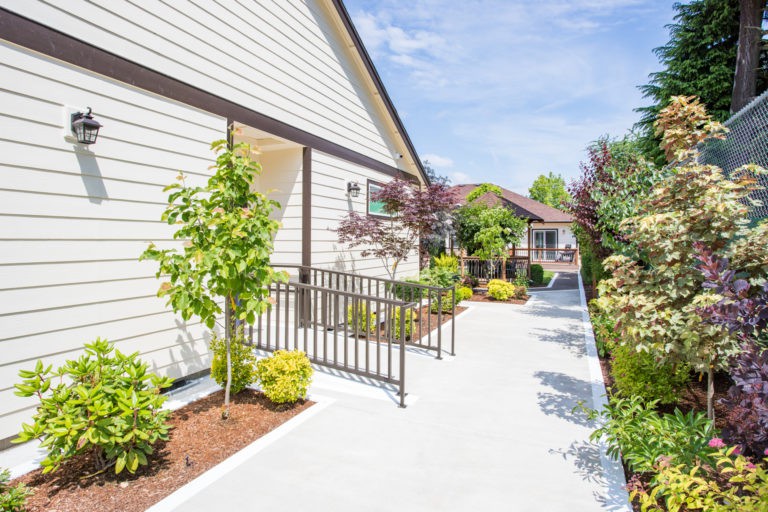 A sidewalk with a ramp and lush landscaping leading to a house on a sunny day.