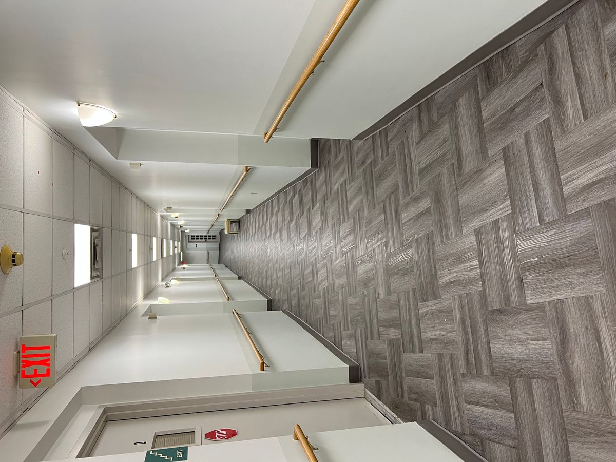 A long, well-lit hallway with gray patterned flooring and handrails on the walls.