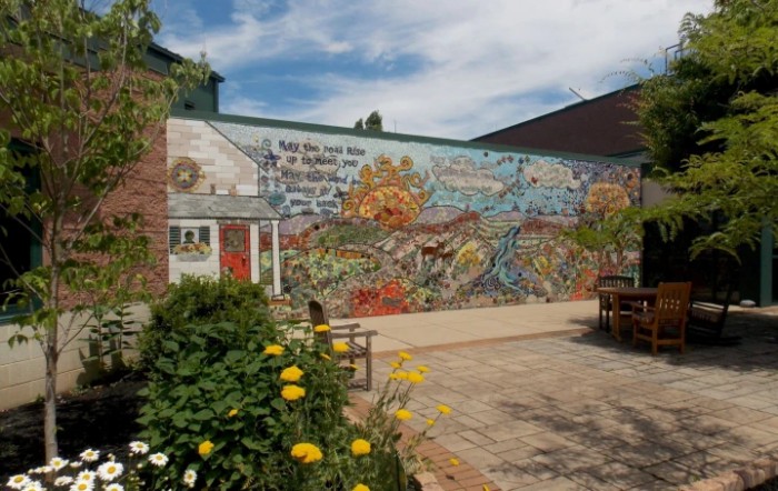 A vibrant mural decorates an outdoor garden area, surrounded by colorful flowers under a clear sky.