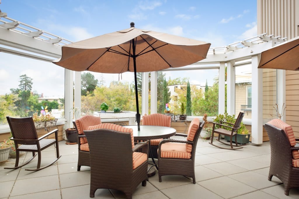 A cozy outdoor patio setup featuring a table with an umbrella and cushioned chairs under a pergola, overlooking a lush garden.