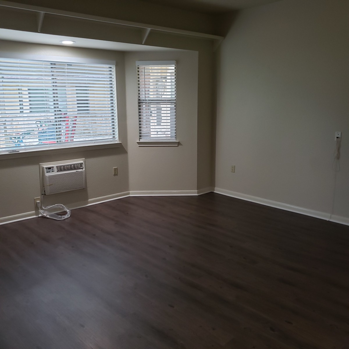 An empty room with dark hardwood floors and large windows.