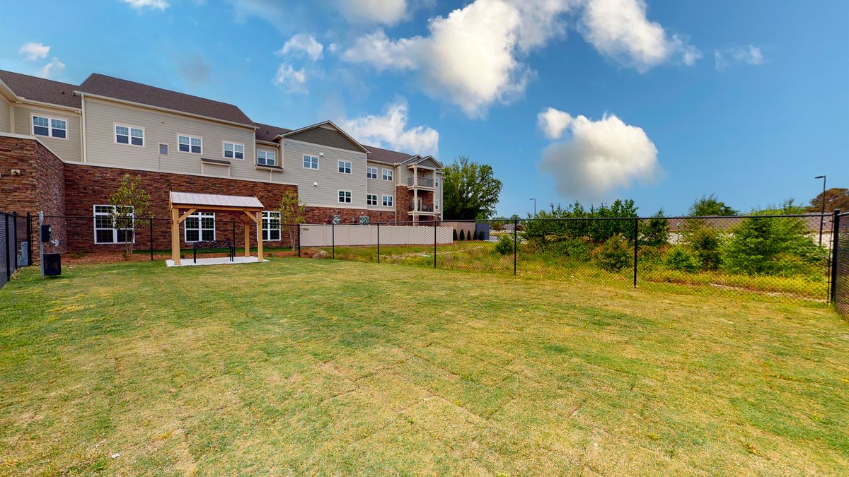 A residential apartment building with a large grassy lawn and a fence under a partly cloudy sky.
