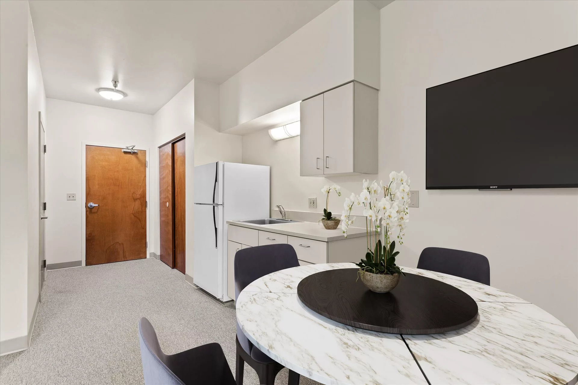 A modern kitchen and dining area featuring a white refrigerator, marble table, and elegant decor.