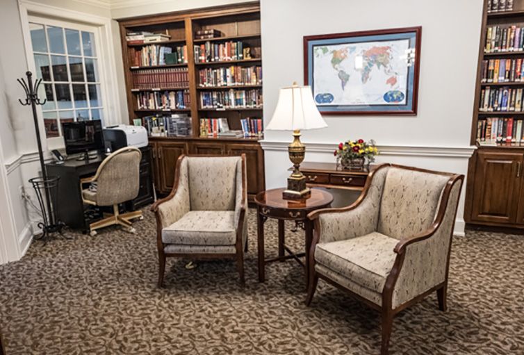 A cozy library nook with bookshelves, comfortable chairs, and a lamp.