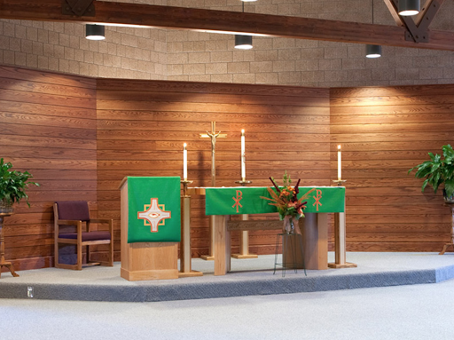 A serene view of a church altar, featuring candles and a green cloth, set against a backdrop of warm wooden walls.