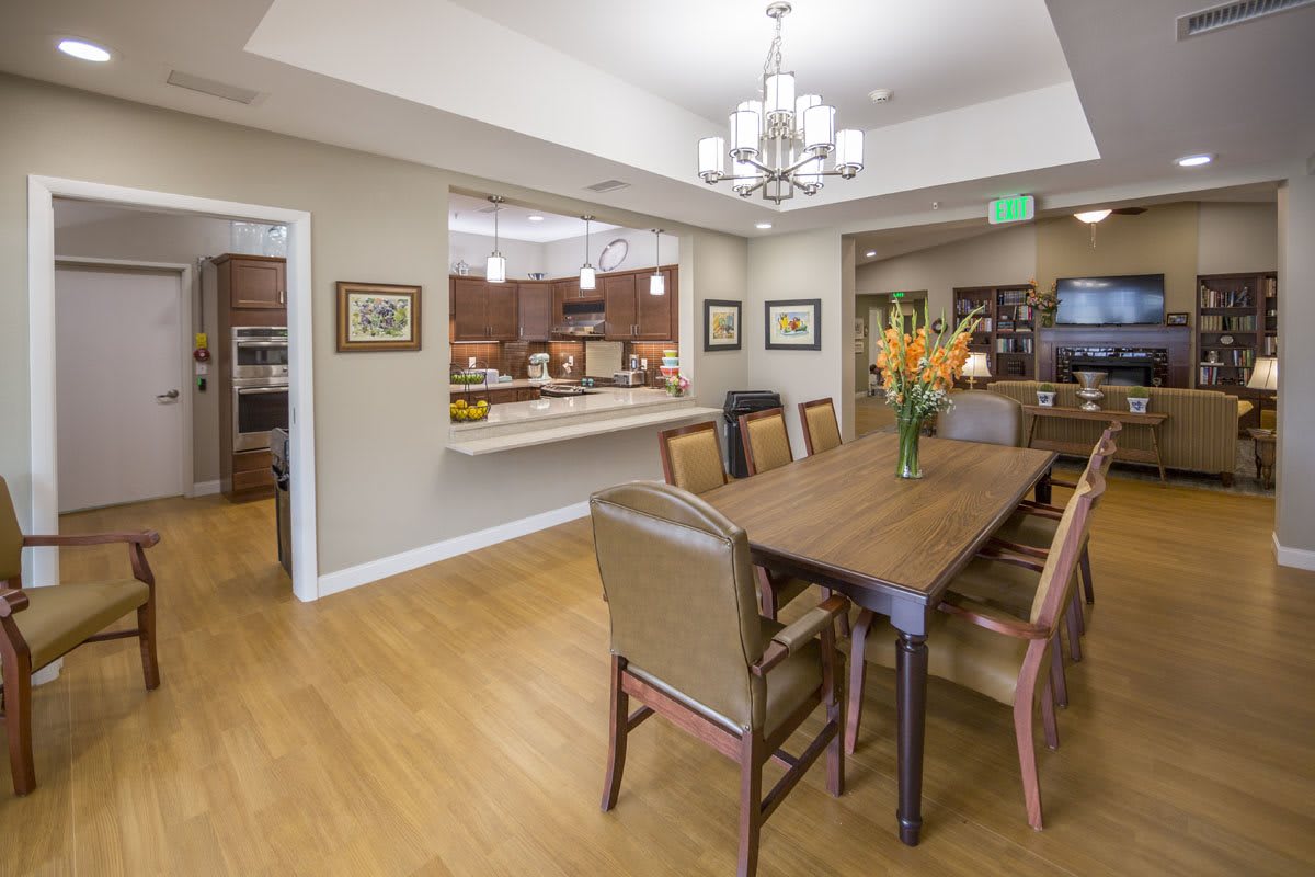 A modern dining room with a wooden table and chairs, featuring an open view to the kitchen area.