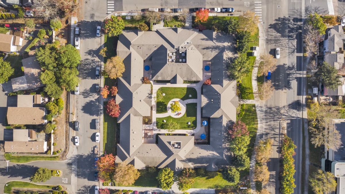 Aerial view of a symmetrical building complex with a central courtyard, surrounded by trees and parking areas.