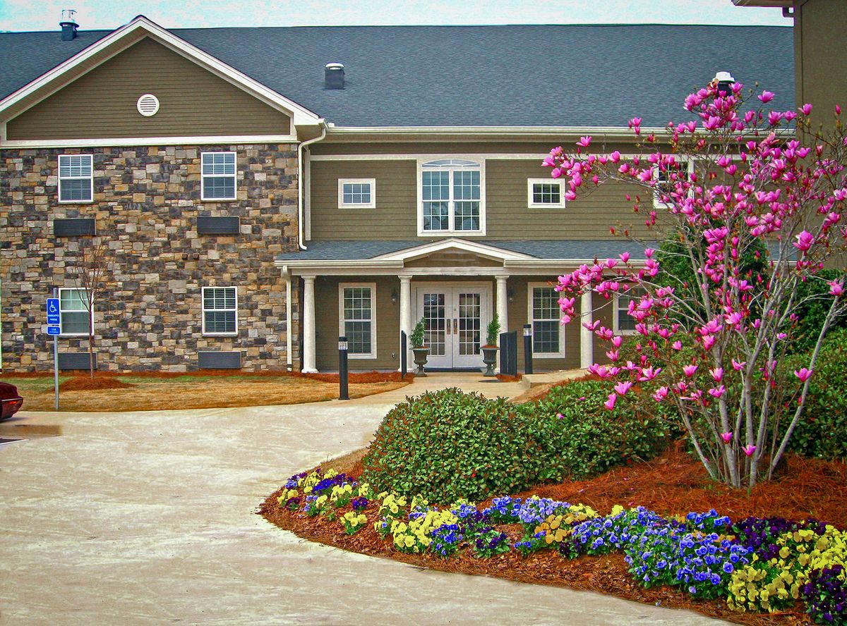 A well-landscaped residential building with a stone facade and vibrant flowers lining the driveway.