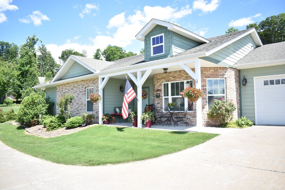 A charming suburban house with a well-maintained lawn and a cozy porch adorned with hanging flower pots, under a clear blue sky.