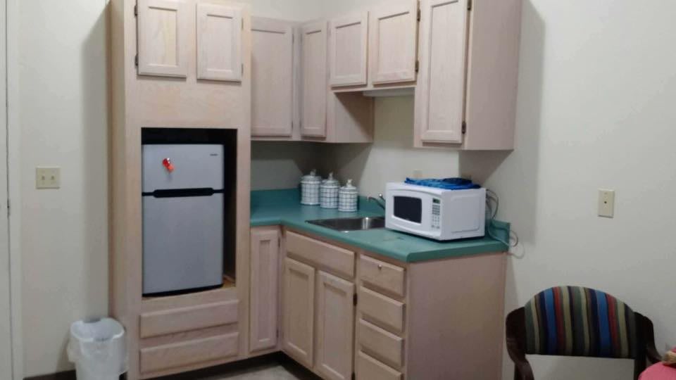 A compact kitchen with beige cabinets, a microwave on the countertop, and a small refrigerator.