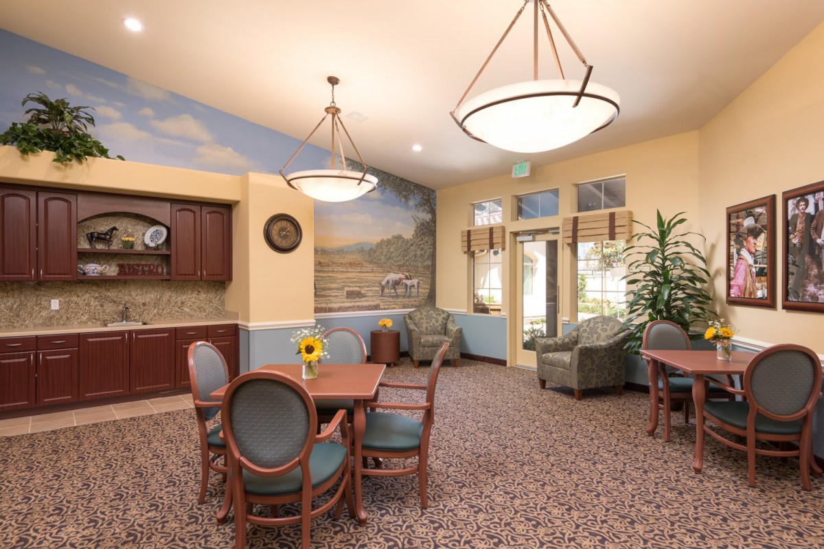 A cozy lounge area with tables, chairs, and comfortable seating, featuring a decorative mural and elegant lighting.