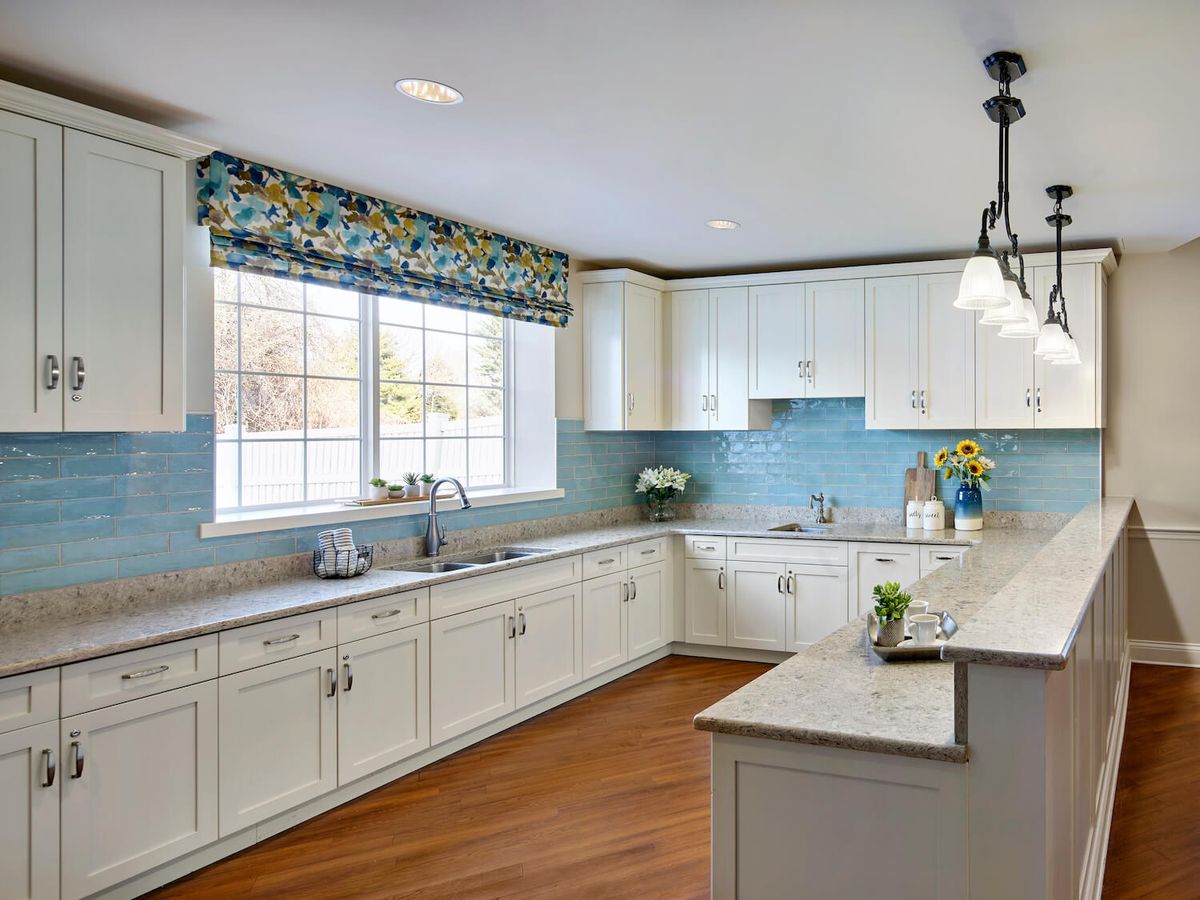 A modern kitchen with white cabinets, wood flooring, and a blue backsplash.